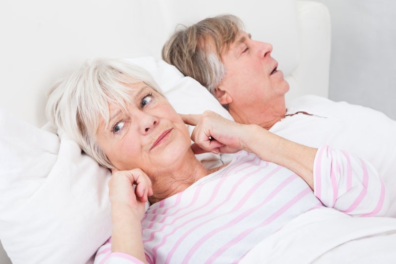 older couple in bed and wife plugging ears because of husband snoring
