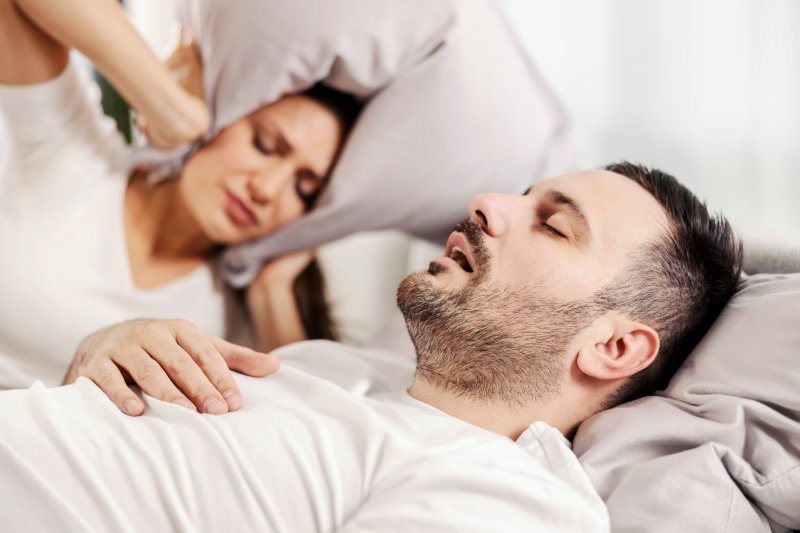 a man snoring and wife covering ears with pillow